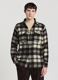 Schwarz-creme kariertes Hemd aus weichem Stoff mit zwei Brusttaschen und Knopfverschluss, getragen über einem beigen Oberteil.