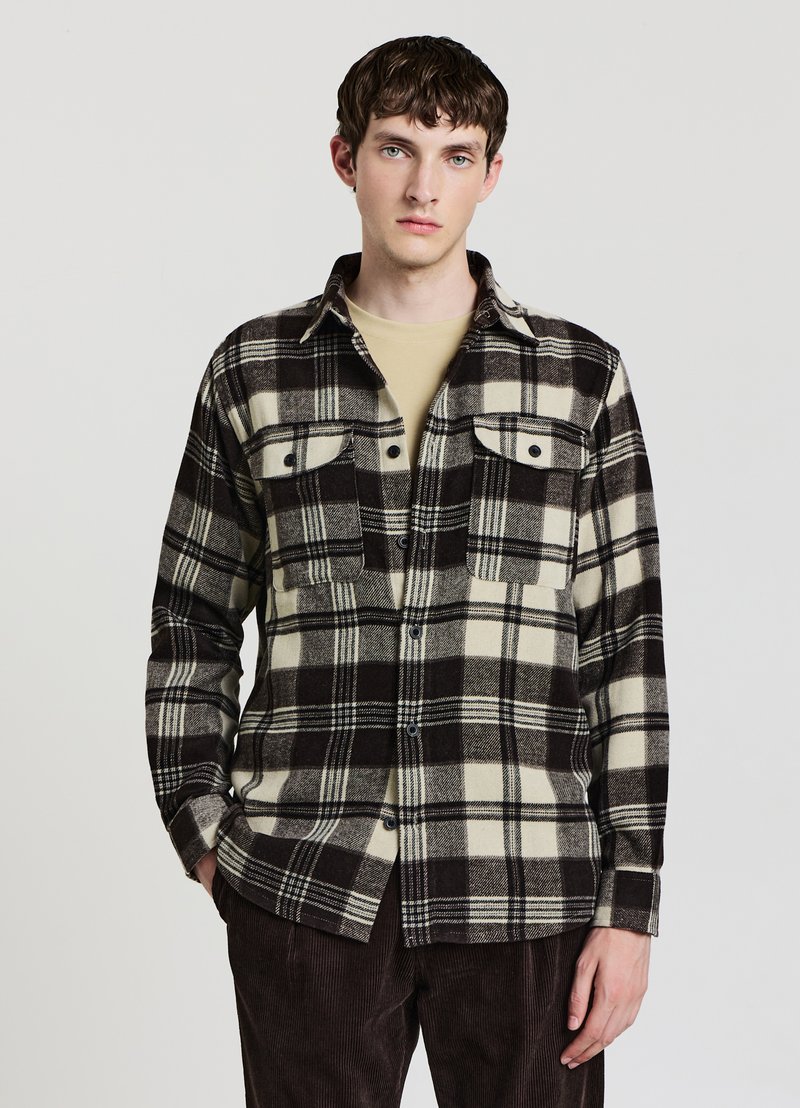Schwarz-creme kariertes Hemd aus weichem Stoff mit zwei Brusttaschen und Knopfverschluss, getragen über einem beigen Oberteil.