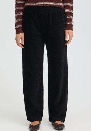 Personne portant un pantalon large en velours côtelé noir, des ballerines marron et un haut rayé bordeaux à manches longues visible de la taille aux pieds.