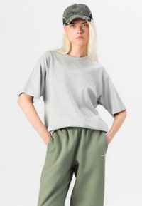 Sivý oversized tričko s diskrétnym logom, spárované s olivovozelenými teplákmi. Oblečenie má voľný strih a jemnú látku.