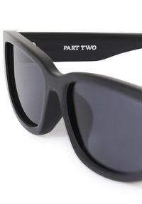 Black oversized sunglasses with dark lenses and "PART TWO" printed in white on the inner side of the temple arm.