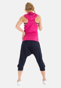 Feszes, rózsaszín, ujjtalan kapucnis pulóver, amely navy harem stílusú nadrággal van párosítva. Sima anyag, cropped fazon, szűkített mandzsettával a bokánál.