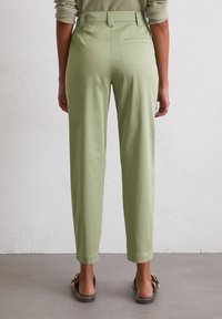 Light green trousers with a high waist, straight leg design, rear pocket detail, and smooth texture. Worn with open-toe sandals.