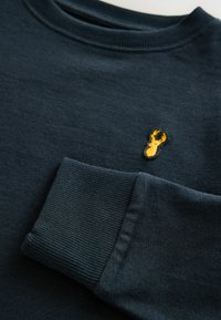 Felpa blu scuro con colletto e polsini a coste, e un piccolo design di un'aragosta ricamata in giallo sul petto. Texture liscia.