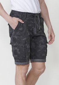Shorts cargo noirs en tissu avec un motif subtil, présentant des poches latérales, une taille à cordon de serrage et des ourlets retroussés.
