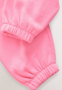 Primo piano di maniche in tessuto rosa con polsini elasticizzati, che mostrano una texture morbida e dettagli di cucitura arricciata.