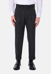 Pantaloni grigi scuri a pieghe in una vestibilità su misura con orli a risvolto e chiusura con un unico bottone, abbinati a scarpe nere lucide.