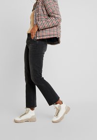 Chaqueta de plumas a cuadros con tonos rojos y negros, camiseta beige, jeans negros de pierna recta y zapatillas altas blancas con suela beige.