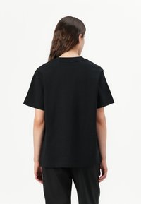 T-shirt en coton noir avec des manches courtes et un col rond. Le dos est simple sans logos ou motifs visibles. Coupe légèrement ample.