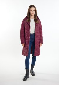 Gequilted kastanjebruine lange jas met een capuchon, zijzakken en een ritssluiting, gecombineerd met blauwe jeans en zwarte enkellaarsjes. Gladde textuur.