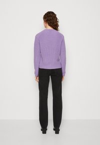 Suéter de punto morado con un diseño ajustado, que presenta una textura de canalé y mangas largas, combinado con pantalones negros de cintura alta.