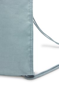 Primo piano dell'angolo di una borsa di tessuto azzurro chiaro con cuciture a punto e sottili corde di chiusura su uno sfondo bianco.