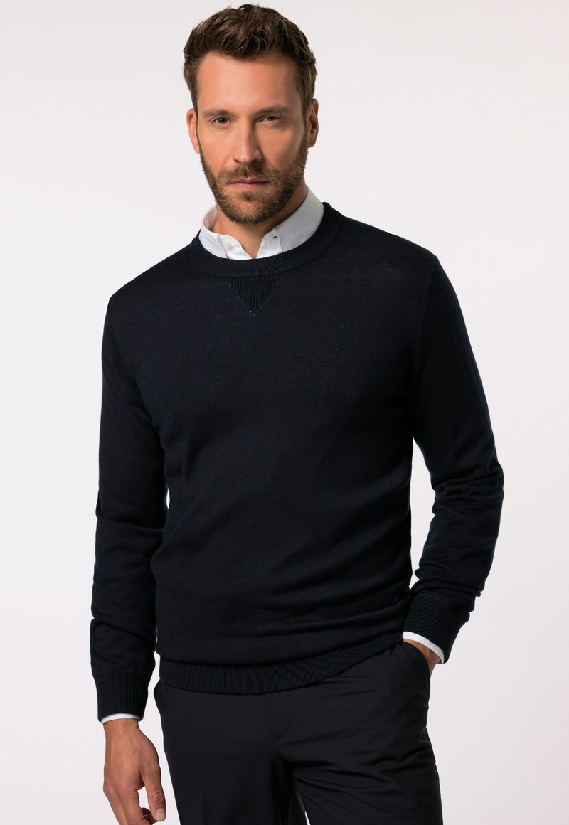 Marineblauer Strickpullover mit rundem Halsausschnitt, gerippten Bündchen und Saum sowie einem strukturierten V-förmigen Akzent auf der Brust. Trägt man über einem weißen Hemd mit Kragen.