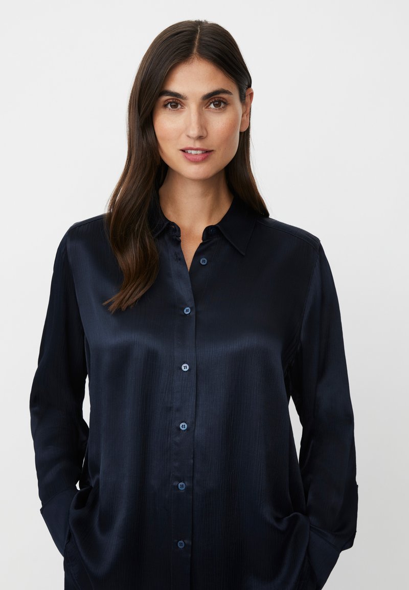 Dunkelblaues Satin-Hemd mit langen Ärmeln und geknöpftem Kragen, das eine glatte Textur und dezenten Glanz aufweist, mit passenden blauen Knöpfen.