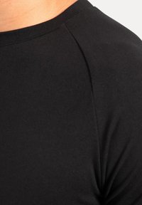 Camiseta negra de manga corta con una textura suave y elástica. Presenta un escote redondeado y un sutil detalle de costura en el hombro.