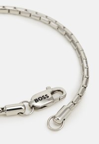 Silver metal chain with rectangular links, featuring a sturdy clasp and a round attachment, marked with "BOSS." Smooth, shiny texture.