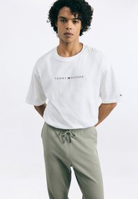 Hvid bomulds T-shirt med "TOMMY HILFIGER" logo i marineblå og rød. Parret med lysegrønne joggers med snøre. Enkel, afslappet stil.