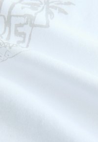 Weißer Stoff mit glatter Textur und dezentem Muster, das hellgraue Elemente aufweist. Das Material wirkt weich und leicht.