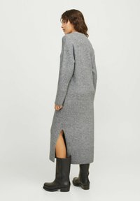 Pilkas megztas suknelė su ilgomis rankovėmis, šoninėmis plyšiais ir raukinėta apačia. Suderinta su ilgais juodais batais, kad sukurtų sluoksniuotą įvaizdį.