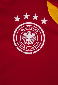 Röd tyg som har en cirkulär logotyp med en vit örn och fyra stjärnor ovanför. Texten säger "Deutscher Fußball-Bund" på ett slätt och hållbart material.