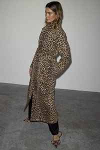 Leopardmønstrete frakk med løs passform, belted midje, lange ermer og sidespalter; kombinert med svarte bukser og matchende sko.