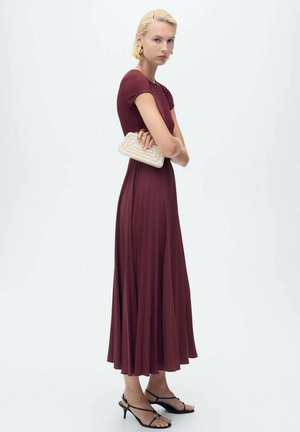 Robe maxi en jersey bourgogne avec manches courtes, forme fluide et pochette texturée crème. Le mannequin porte des sandales noires à lanières.