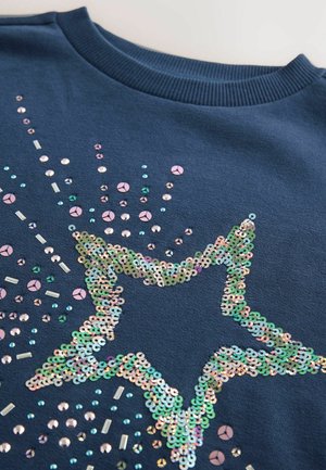 Sweatshirt bleu marine avec un grand design d'étoile composé de sequins multicolores et d'accents en perles, mettant en valeur une surface texturée et brillante.