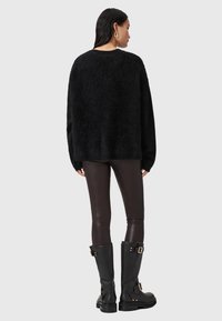 Czarny, puszysty sweter o luźnym kroju, z długimi rękawami i ściągaczem na dole, w połączeniu z brązowymi legginsami z imitacji skóry i wysokimi, czarnymi botkami.