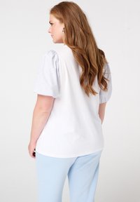 T-shirt blanc avec des manches bouffantes rayées bleu clair. Matière en coton doux. Coupe décontractée. À assortir avec un pantalon bleu clair. Pas de motifs ou d'accents visibles.
