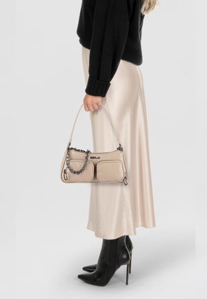 Borsa beige con due tasche frontali, dettaglio a catena e tracolla regolabile, abbinata a un maglione nero e una gonna in crema simile alla seta.