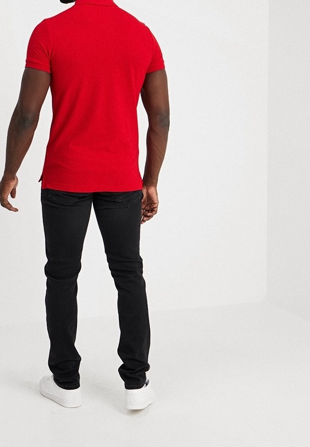 Rotes kurzärmliges Poloshirt mit Kragen, kombiniert mit schwarzen Slim-Fit-Jeans und weißen Sneakers, von hinten betrachtet.