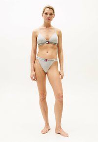 Bralette et string en coton gris avec des fines bretelles, comportant une bande logo de couleurs rouge, blanc et bleu, au design minimaliste.
