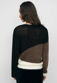 Kootud sviiter, millel on musta, pruuni ja kreemika värvi plokkdisain, samuti pehme valge äär ja tekstuuriga kangas.