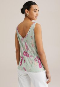 Cvetlična majica brez rokavov v svetlo zeleni tkanini, z V-izrezom in pisanimi rožnatimi ter vijoličnimi cvetličnimi vzorci, sproščenega kroja in ukrivljenim robom.