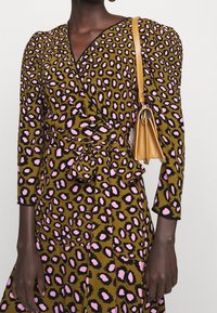 Leopardenmuster Wickelkleid in Oliv mit rosa Akzenten; verfügt über lange Ärmel, einen Taillengürtel und eine strukturierte Oberfläche. Begleitet von einer hellbraunen Tasche.