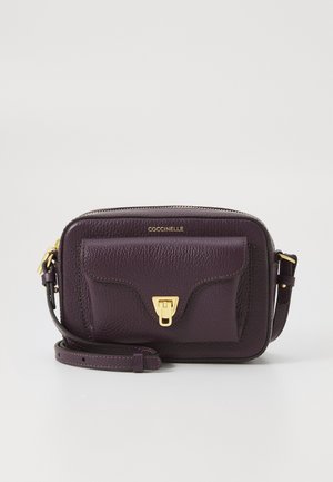 Sac bandoulière en cuir texturé violet foncé avec poche avant, fermoir doré, bandoulière ajustable et nom de marque doré "Coccinelle" au centre en haut.