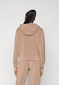 Felpa color corda con un fit rilassato, texture morbida e un grande cappuccio. Presenta polsini e vita a coste per una vestibilità aderente.