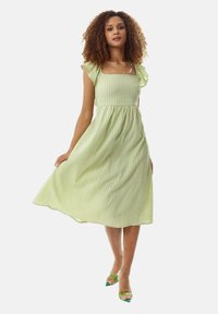 Green and white striped midi dress with a square neckline, ruffled shoulder sleeves, and a flared skirt. Worn with green heels.
