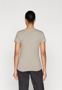 Εφαρμοστό κοντομάνικο μπλουζάκι από βαμβάκι σε ανοιχτό μπεζ χρώμα, με στρογγυλή λαιμόκοψη και διακριτική καμπυλωτή ραφή στο τελείωμα, φορεμένο με σκούρο παντελόνι.