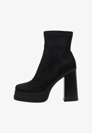 Botín de ante negro con un alto tacón de bloque, punta redondeada y parte superior elástica. Textura suave, diseño elegante y suela de plataforma para mayor altura.