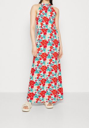 Ärmeløs maxikjole med høj halsudskæring, med et levende rødt og grønt blomsterprint på en lys baggrund, kombineret med beige sandaler med rynket detalje.