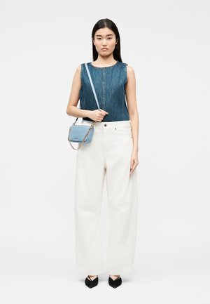 Γυναίκα που φοράει αμάνικο τοπ από τζιν, ψηλόμεσο φαρδύ λευκό παντελόνι, μαύρα μυτερά παπούτσια και κρατάει μικρό μπλε τσαντάκι ώμου με αλυσίδα.