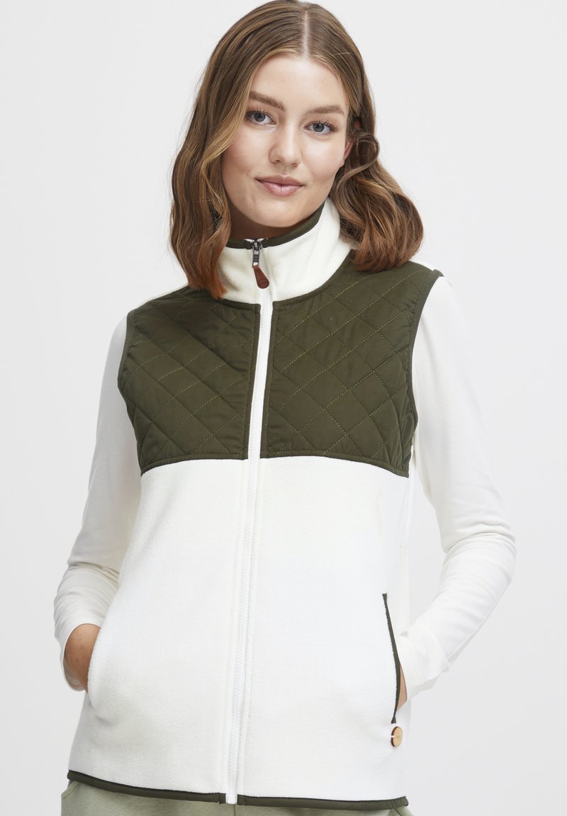 Balts un olīvzaļš veste ar quilted dizainu, augstu apkakli, priekšējo rāvējslēdzēju un divām sānu kabatām. Gluda tekstūra ar kontrastējošu šuvju.