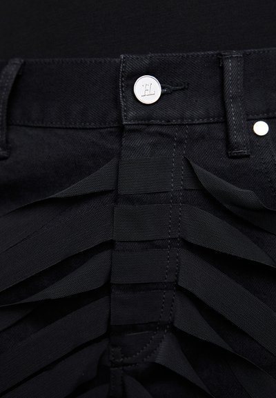 Pantalons en denim noir avec un design unique, présentant des sangles élastiques noires disposées en couches le long du panneau avant. Accents en matériaux argentés.