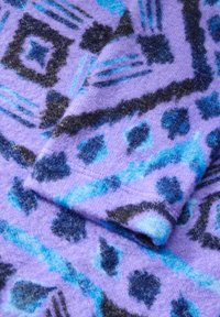 Paarse stof met blauwe en zwarte abstracte patronen, zachte textuur en een gevouwen sectie die overlappende ontwerpelementen onthult.