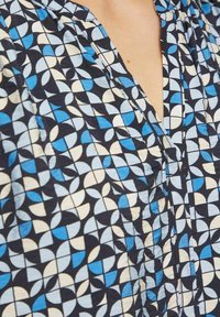 Blauwe en crème gestreepte stof met geometrische vormen op een marineblauwe achtergrond. Het ontwerp bevat verschillende gebogen en hoekige vormen.