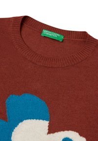 Gestrickter Pullover in rostrot mit blauem und weißen Blumendesign. Verfügt über einen gerippten Rundhalsausschnitt und ein Etikett "United Colors of Benetton".