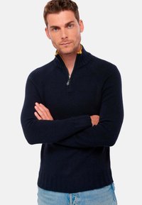 Pull à col zippé bleu marine avec col et poignets côtelés. Fabriqué en tissu texturé avec un col intérieur contrastant. Design ajusté.
