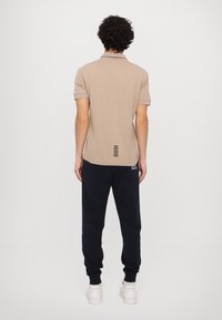 Beige polo shirt with short sleeves and black accents, paired with dark navy sweatpants and white sneakers. Features horizontal stripe detail on back.