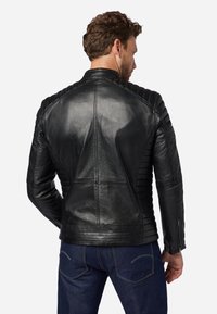Svart lädermotorcykeljacka med kviltade axelaccenter, en figursydd design och minimalistiska sömmar. Slät textur med matt finish.